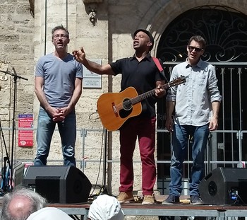 DAVY KILEMBÉ, SUR LA PLACE   Place Gambetta, plein soleil, une scène, un chanteur, deux musiciens. Davy Kilembé nous emmène en voyage. Nous sommes bien au delà des murs anciens qui entourent cette place, et rejoignons le ciel bleu pour aller au pays où les hanches se balancent, où les corps tanguent, il y a quelque chose dans l'air qui chaloupe et nous fait du bien. La chanson de Davy Kilembé est avant tout un son aux accents des Caraïbes. Et que ce soit de la ballade ou des morceaux plus festifs, partout il développe cette pulsation profonde, ce goût du bonheur d'une musique colorée où les vibrations rapproche les hommes. Pour cela, il joue merveilleusement bien de la guitare et de la voix et est magnifiquement accompagnés par Eric Flandrin à la batterie et Guillaume Bouthié à la contrebasse. Mais, chez Davy Kilembé, tout ne se résume pas à la musique. Comme un contrepoint, nombre de ses textes sont empreint d'une douce mélancolie. Il évoque non sans humour le temps de La 4L à Momo, « Dans le trou » nous retrouvons des jeunes ados autour de la tombe de Jim Morisson, il y a aussi cette maison où « Il y a longtemps, il y avait des gens ». Il nous donne à partager des moments d'humanité et toujours avec ce son qui sonne et des refrains diablement efficaces. Le public reprend avec lui ses mots car il « Dit les mots » qu'il faut. Et même si dans « Mon pays », Davy Kilembé est « Un petit noir » moi je dis bravo. Ces origines transpirent sur scène, dans sa musique, dans ses textes et aussi dans sa façon d'être là simplement avec nous et de nous redonner la joie. BRUNO HILDESHEIM