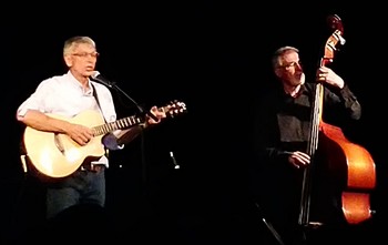 En première partie, Alain Chataignier « J’ai pris le pas du baladin / Et j’en appelle aux musiciens / Qui ont la musique dans la main… » Lui, Alain Chataignier, qui réside dans les Deux-Sèvres, est un inconnu, peut-être plus encore que les autres. Car sans trace discographique. Il a l’âge et l’art d’être grand-père : il l’est. On s’imagine sans le savoir qu’il a depuis toujours écouté de la chanson française, aimé ses pairs. Sans s’en inspirer plus que ça, il porte l’ADN de tous les chanteurs à la guitare, avec ou sans pipe. Tout inconnu qu’il est, il se chante, en une autobiographie sincère et séduisante. De son grand-père mort dans les tranchées (en une brillante chanson très antimilitariste, de celles qu’on verrait bien entonnées au monument aux morts, un 11 novembre, et devant le siège social de chez Dassault : « C’est malheureux de partir se faire tuer / alors qu’il y a tant à faire / Pour engranger le blé ») à ce grand-père qu’il est à son tour devenu. On ne parlera pas de saga familiale mais c’en est l’agréable esquisse : toute sa vie il a semé des graines et de belles chansons ont poussées. Très classiques dans la forme et le rendu, mais pas sans impertinence, ni érotisme parfois, comme dans ce Sommelier qui ajoute cette dimension à la belle ivresse d’un bon cru. Belle prestation, sobre, efficace, chaleureuse. Avec pour complice un autre Alain (Largeot) à la contrebasse comme à la trompette. Un tel répertoire ne bouleverse certes pas les codes de la chanson : n’empêche qu’il ajoute une pierre très respectable et agréable à cet art. Tant qu’on se dit que c’est dommage que cet auteur compositeur et interprète soit passé à côté des radars (et trompettes) de la renommée. Modeste, quasi effacé, il est un simple mais probant artisan de la chanson.